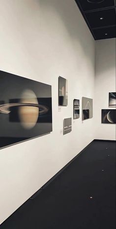 an art gallery with black and white photographs on the wall, saturn in the background