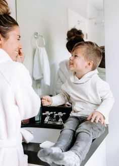 a little boy sitting on top of a counter next to a woman in a bathrobe