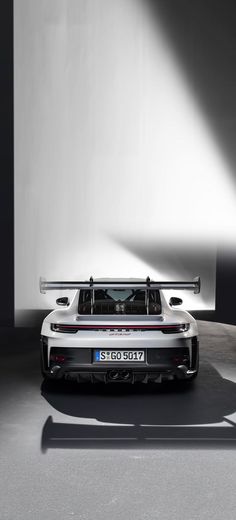 the rear end of a white sports car in a dark room with light coming from behind it