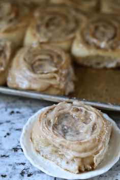 cinnamon rolls sitting on top of a white plate next to a baking pan filled with them