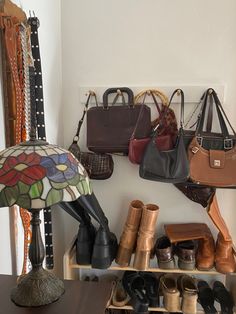 several purses and handbags are hanging on the wall next to a table lamp