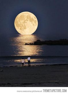 two people standing on the beach watching the moon