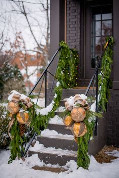 two wreaths with pine cones and evergreen leaves are on the front steps of a house