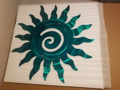 a green and white metal sun decoration on a cardboard box in the shape of a spiral