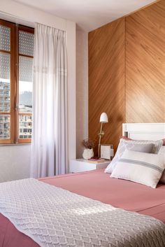 a bed with pink sheets and pillows in a bedroom next to a wooden headboard