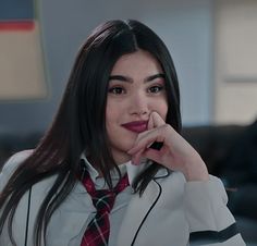 a woman with long hair wearing a white shirt and red tie sitting in front of a couch