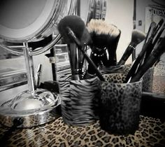 several makeup brushes are sitting in a cup on a leopard print table cloth next to a mirror