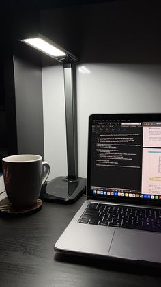 an open laptop computer sitting on top of a desk next to a coffee cup and lamp