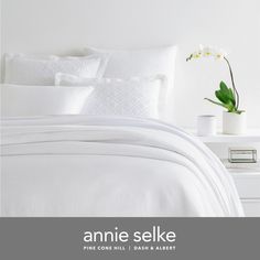 a bed with white sheets and pillows in a bedroom next to a vase filled with flowers