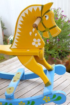 a yellow rocking horse with flowers painted on it's body and head, sitting on a wooden deck