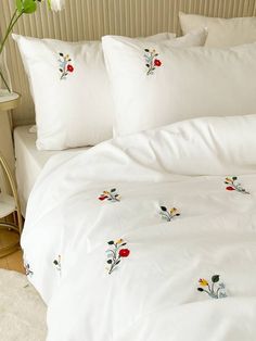 a white bed topped with lots of pillows next to a night stand and table filled with flowers