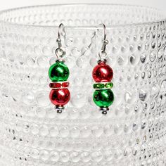 two red and green christmas balls are hanging from silver earwires on a clear glass background