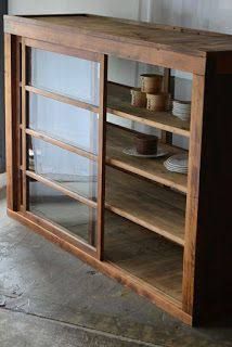 a wooden cabinet with glass doors and plates on the bottom shelf, in front of a white wall