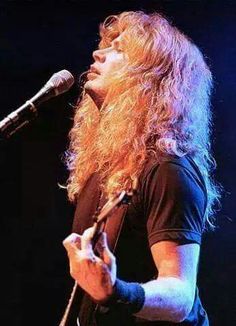 a man with long hair holding a guitar in front of a microphone and singing into a mic