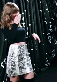 a woman standing in front of a curtain with her hand on her mouth and wearing black boots