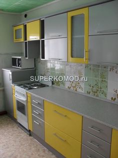 a kitchen with yellow and gray cabinets, silver counter tops, and white tile backsplash