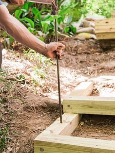 a man holding a hammer over some wooden planks on the ground in front of trees