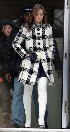 a woman in black and white coat walking out of a building with her hands on her hips