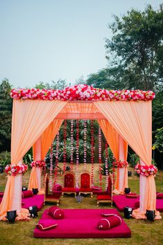 an outdoor wedding setup with pink and orange flowers on the altar, white drapes and red pillows