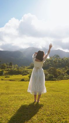 a woman in a white dress standing on top of a lush green field under a blue sky