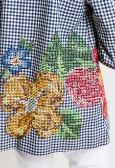 a woman wearing a blue and white checkered shirt with flowers on the front,