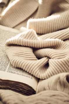 an open book laying on top of a bed covered in blankets and mittenss