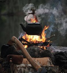 a tea kettle is on fire in the middle of some wood and logs with an ax sticking out of it