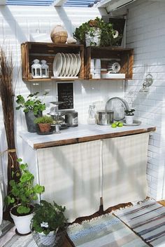 an outdoor kitchen with pots and pans on the shelves, potted plants in vases