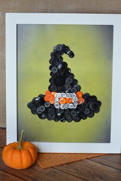 an orange pumpkin sitting on top of a wooden table next to a photo frame with buttons in the shape of a witch's hat
