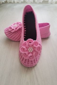 pink crocheted baby shoes with flowers on the toes and bottom, sitting on a white surface