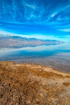 an aerial view of a lake and mountains in the distance with blue skies above it