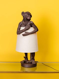 a lamp with a monkey holding a paper towel on it's arm, against a yellow wall