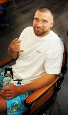 a man sitting in a chair holding a water bottle and pointing to the side with his finger