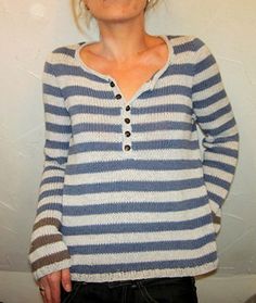 a woman standing in front of a white wall wearing a blue and gray striped sweater