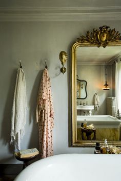 a bath tub sitting under a large mirror next to a sink in a bathroom with a gold framed mirror on the wall