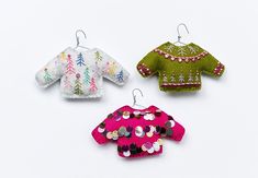 three knitted sweaters hanging from hooks on a white surface, one with buttons and the other with sequins