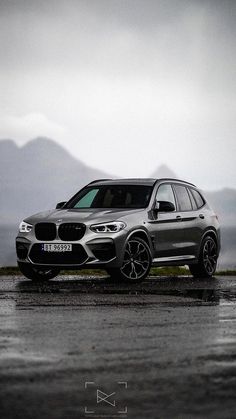 a grey bmw suv parked on the side of a road with mountains in the background