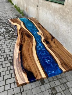 a table made out of wood with blue water in the center on a brick sidewalk