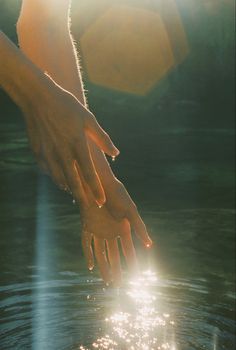 two hands reaching for each other in the water with sunlight shining on them and behind them