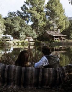 two people sitting on a couch looking out over the water at a camper in the background