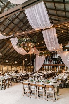 an indoor wedding venue with white draping and wooden tables set up for dinner