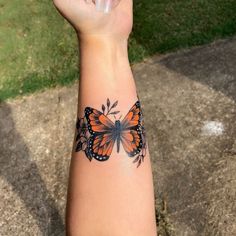 a woman's arm with an orange and black butterfly tattoo on her left wrist