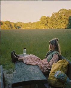 a woman sitting on top of a wooden bench next to a picnic table in a field
