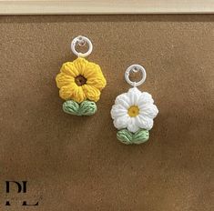 two flower earrings are hanging from hooks on a brown surface, one is yellow and the other is white