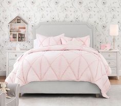 a bed with pink comforter and pillows in a bedroom next to a white dresser