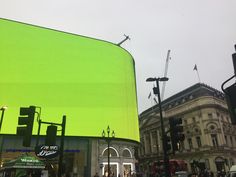 a large green screen on the side of a building next to traffic lights and pedestrians