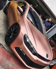 a pink sports car parked in front of a garage door with people looking at it