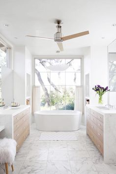 a white bathroom with marble flooring and large windows overlooking the trees in the distance