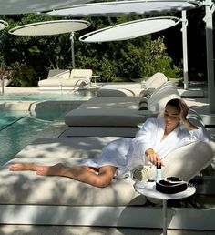 a woman laying on top of a white chair next to a pool