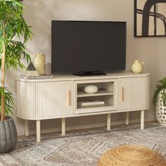 a flat screen tv sitting on top of a white entertainment center next to a potted plant